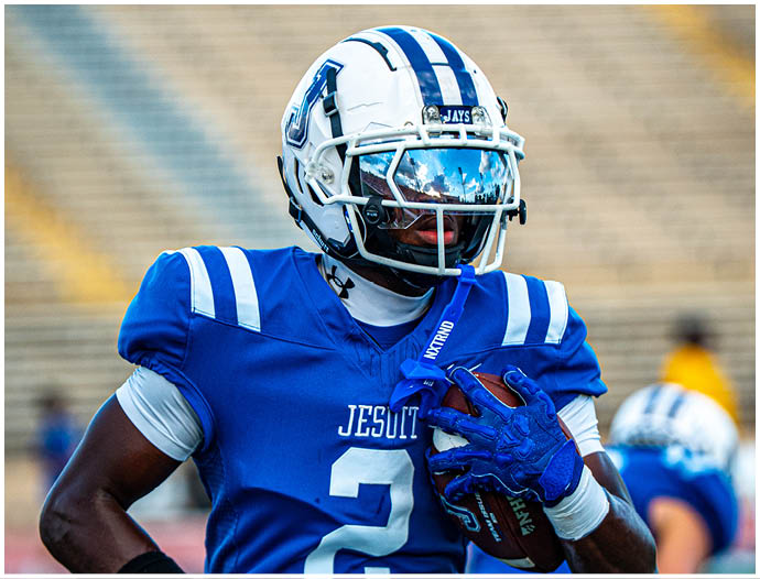 Three football players in blue and white uniforms running on a field. Description generated by AI