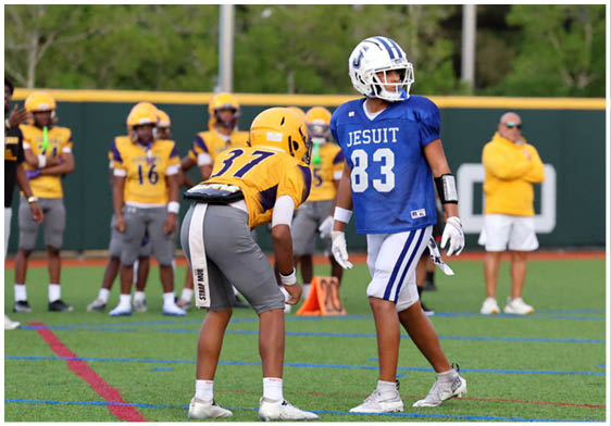 Three football players in blue and white uniforms running on a field. Description generated by AI