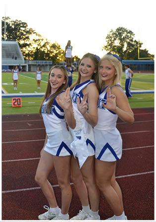 Three football players in blue and white uniforms running on a field. Description generated by AI