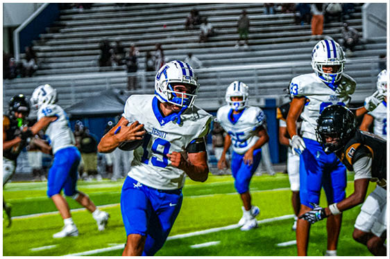 Three football players in blue and white uniforms running on a field. Description generated by AI