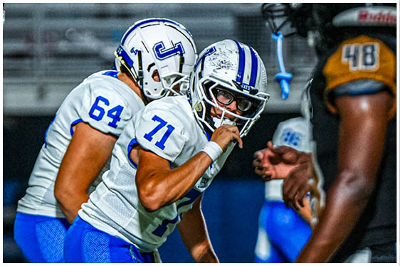 Three football players in blue and white uniforms running on a field. Description generated by AI
