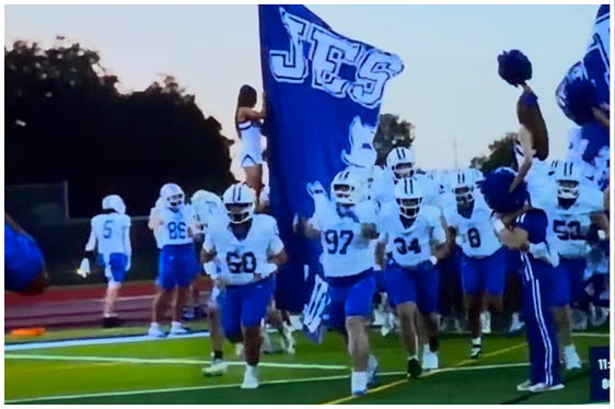 Three football players in blue and white uniforms running on a field. Description generated by AI