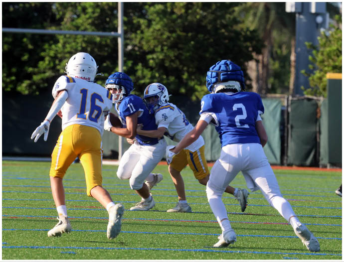 Three football players in blue and white uniforms running on a field. Description generated by AI