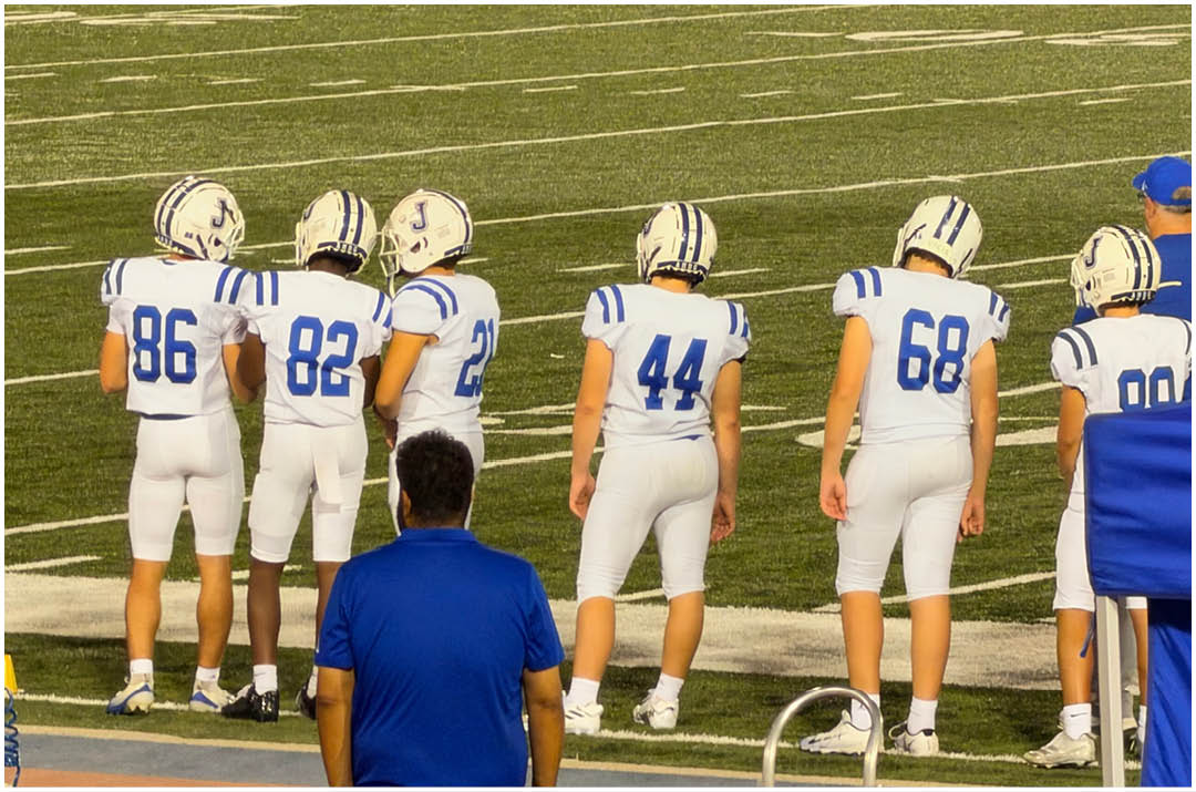 Three football players in blue and white uniforms running on a field. Description generated by AI