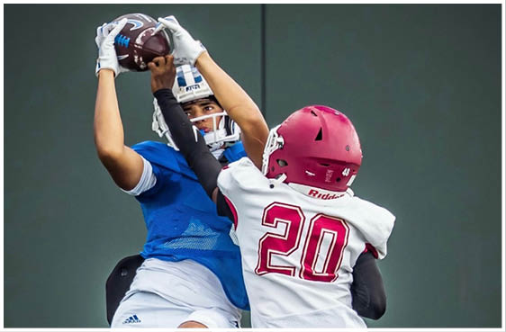 Three football players in blue and white uniforms running on a field. Description generated by AI