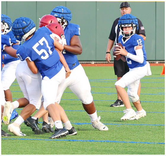 Three football players in blue and white uniforms running on a field. Description generated by AI