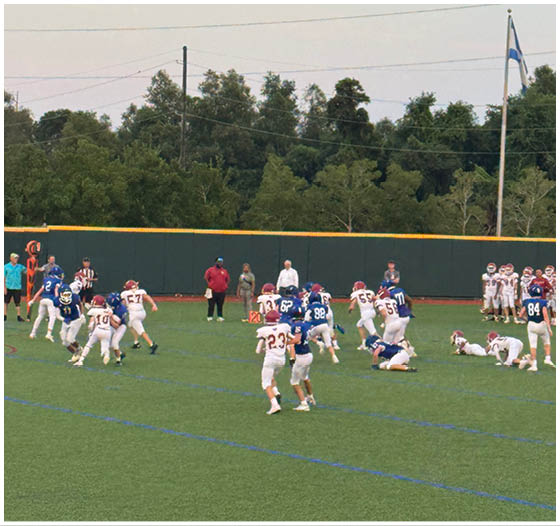 Three football players in blue and white uniforms running on a field. Description generated by AI