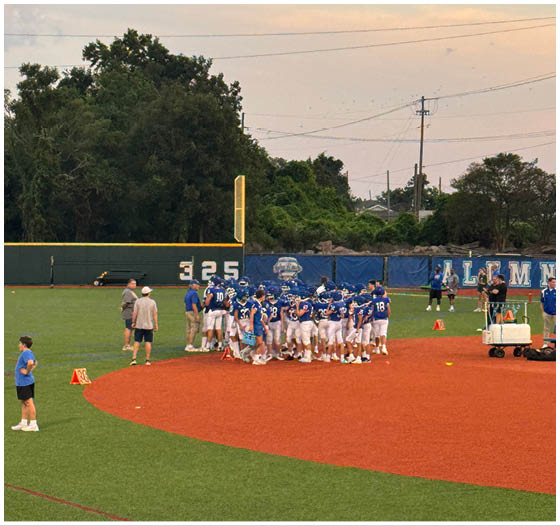 Three football players in blue and white uniforms running on a field. Description generated by AI
