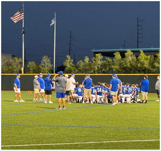 Three football players in blue and white uniforms running on a field. Description generated by AI