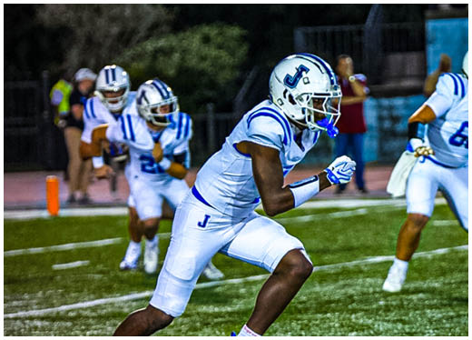 Three football players in blue and white uniforms running on a field. Description generated by AI
