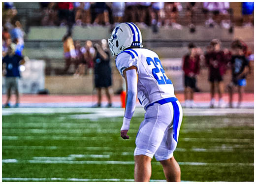 Three football players in blue and white uniforms running on a field. Description generated by AI