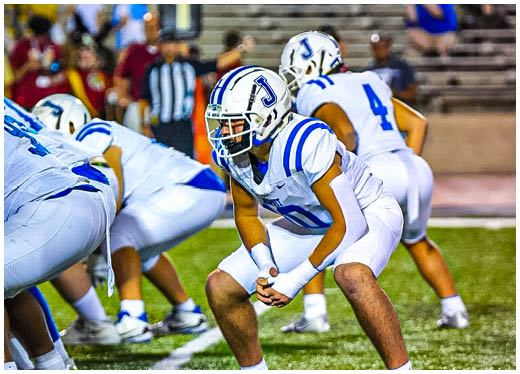 Three football players in blue and white uniforms running on a field. Description generated by AI