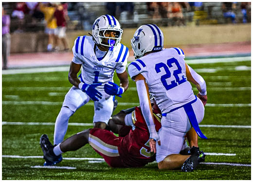 Three football players in blue and white uniforms running on a field. Description generated by AI