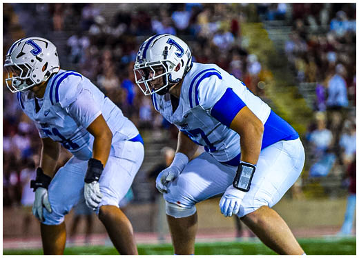 Three football players in blue and white uniforms running on a field. Description generated by AI