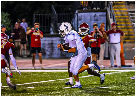 Three football players in blue and white uniforms running on a field. Description generated by AI