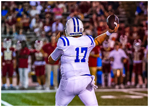 Three football players in blue and white uniforms running on a field. Description generated by AI