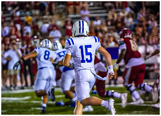 Three football players in blue and white uniforms running on a field. Description generated by AI