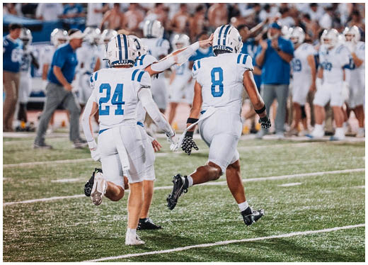 Three football players in blue and white uniforms running on a field. Description generated by AI