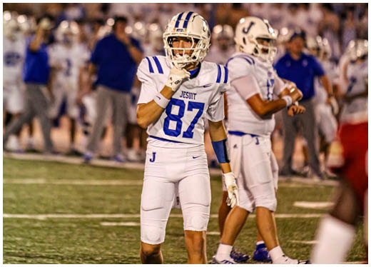 Three football players in blue and white uniforms running on a field. Description generated by AI