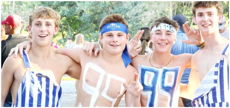 Three football players in blue and white uniforms running on a field. Description generated by AI