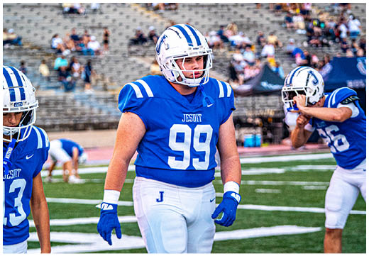 Three football players in blue and white uniforms running on a field. Description generated by AI