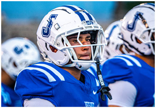 Three football players in blue and white uniforms running on a field. Description generated by AI
