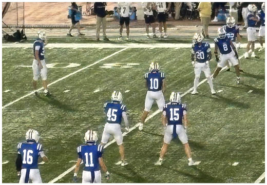Three football players in blue and white uniforms running on a field. Description generated by AI