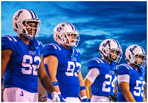 Three football players in blue and white uniforms running on a field. Description generated by AI