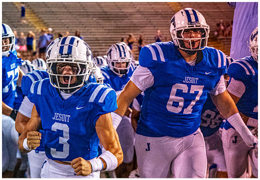 Three football players in blue and white uniforms running on a field. Description generated by AI