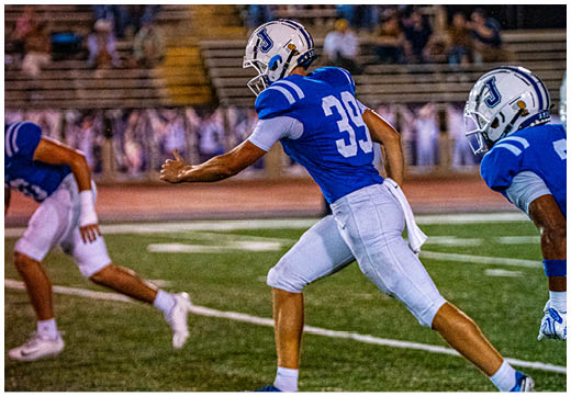 Three football players in blue and white uniforms running on a field. Description generated by AI
