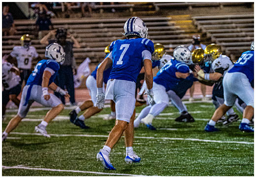 Three football players in blue and white uniforms running on a field. Description generated by AI
