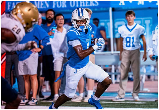 Three football players in blue and white uniforms running on a field. Description generated by AI
