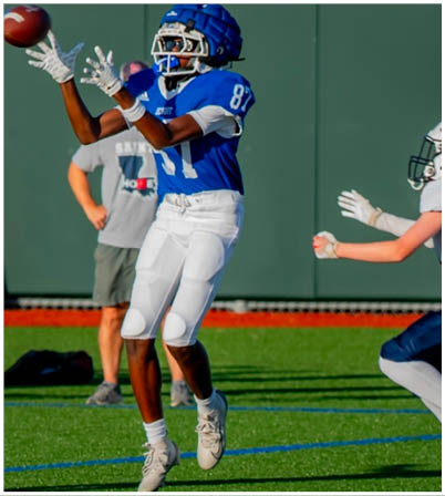 Three football players in blue and white uniforms running on a field. Description generated by AI