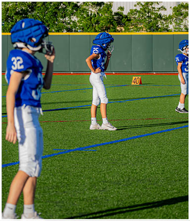 Three football players in blue and white uniforms running on a field. Description generated by AI