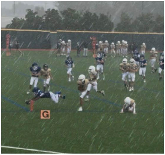 Three football players in blue and white uniforms running on a field. Description generated by AI