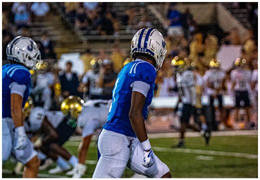 Three football players in blue and white uniforms running on a field. Description generated by AI