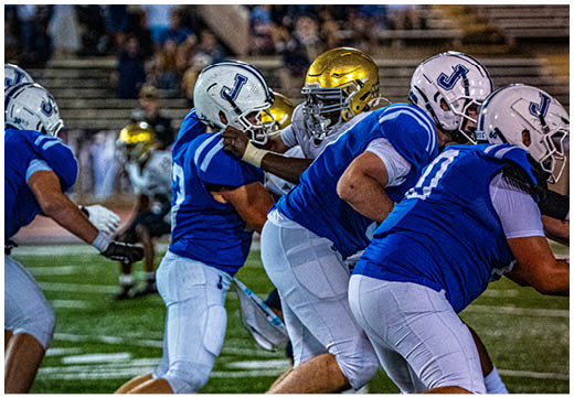 Three football players in blue and white uniforms running on a field. Description generated by AI