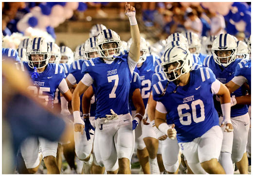 Three football players in blue and white uniforms running on a field. Description generated by AI