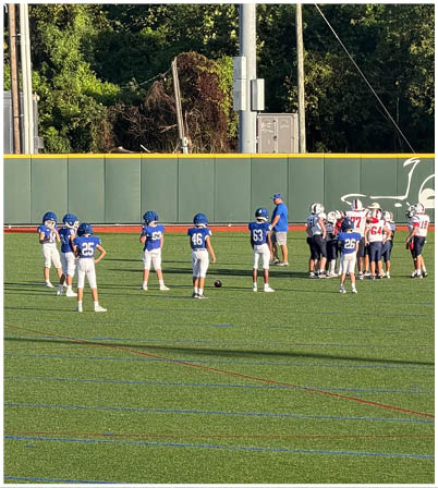 Three football players in blue and white uniforms running on a field. Description generated by AI