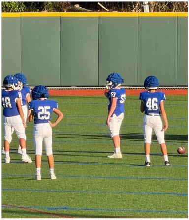 Three football players in blue and white uniforms running on a field. Description generated by AI