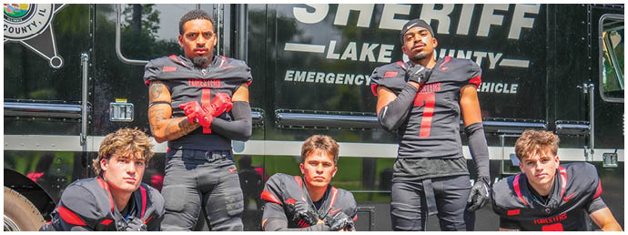 A group of football players pose in front of a sheriff's truck. Description generated by AI