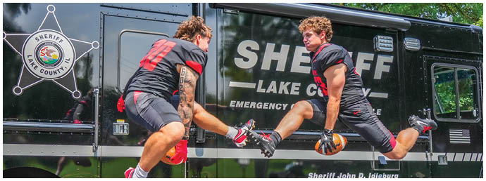 Two men jumping in front of a sheriff's lake truck. Description generated by AI