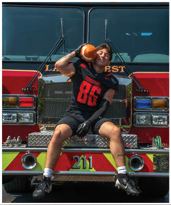 A man is sitting on the front of a fire truck. Description generated by AI