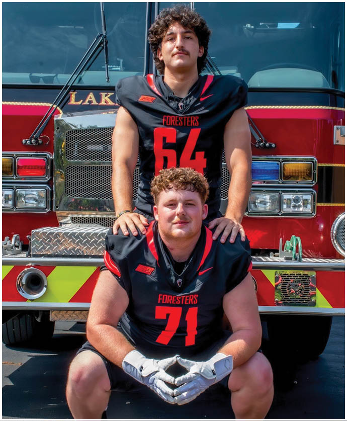 Two football players pose in front of a fire truck. Description generated by AI