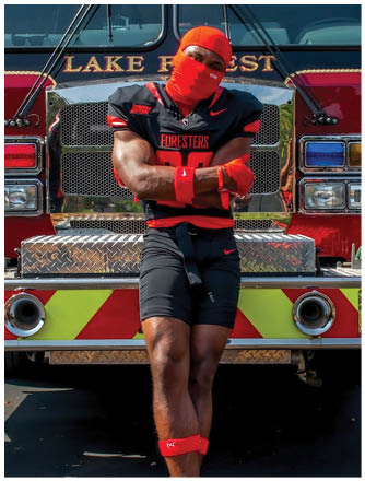 A man wearing a red and black jersey and a red bandana is leaning against a fire truck. Description generated by AI