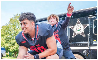 Two men playing football in front of a truck. Description generated by AI