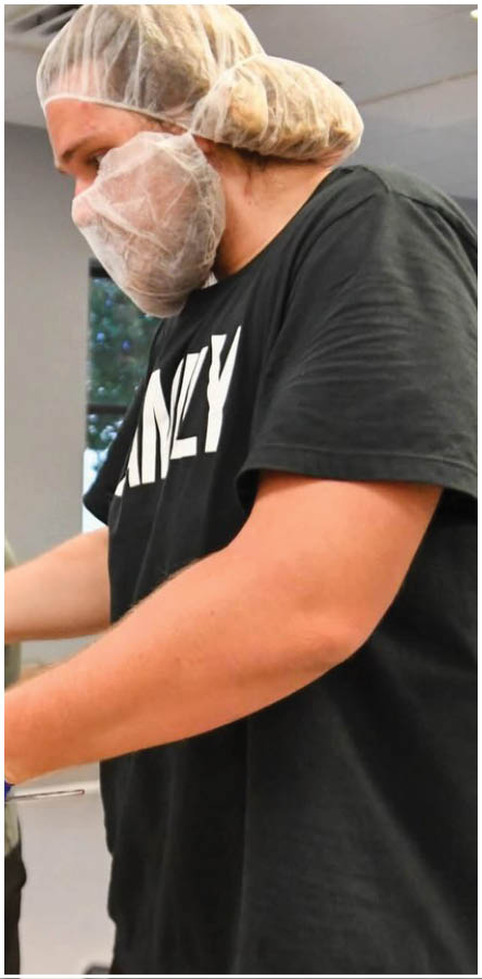 A group of people wearing hairnets and gloves are preparing food. Description generated by AI