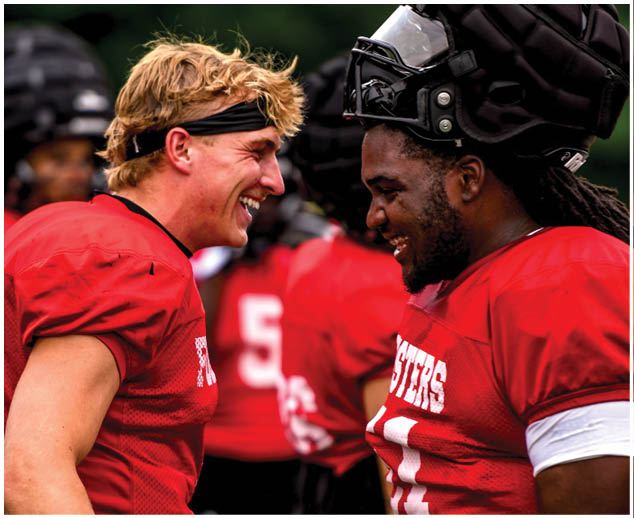 Two men wearing red jerseys are laughing and talking to each other. Description generated by AI