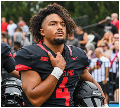 A football player wearing a black jersey with the number 4 on it. Description generated by AI
