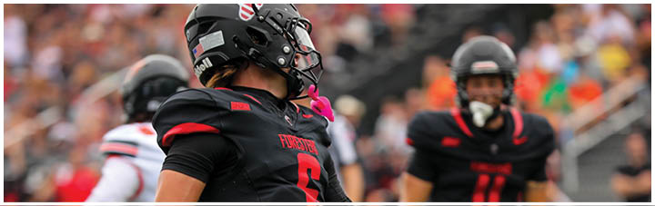 A football player wearing a black jersey with the number 12 on it. Description generated by AI